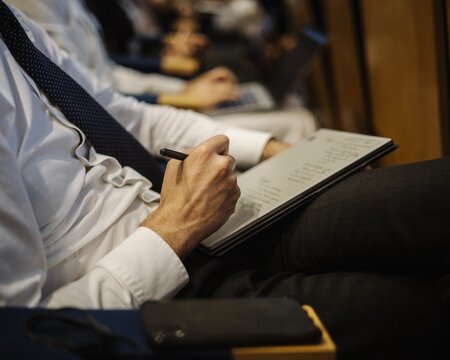 a man in a shirt and tie writing notes at a meeting