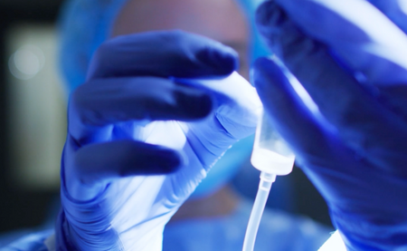 two hands in surgical gloves holding an IV drip
